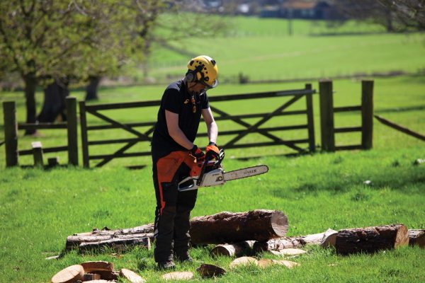 Bicton College Arboriculture students chopping up tree branches with a chainsaw in a field