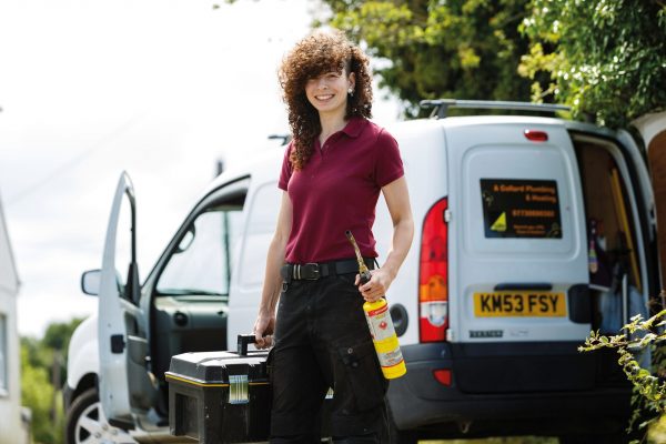Plumbing alumni Alice Collard stands in front of her van holding her tool kit.