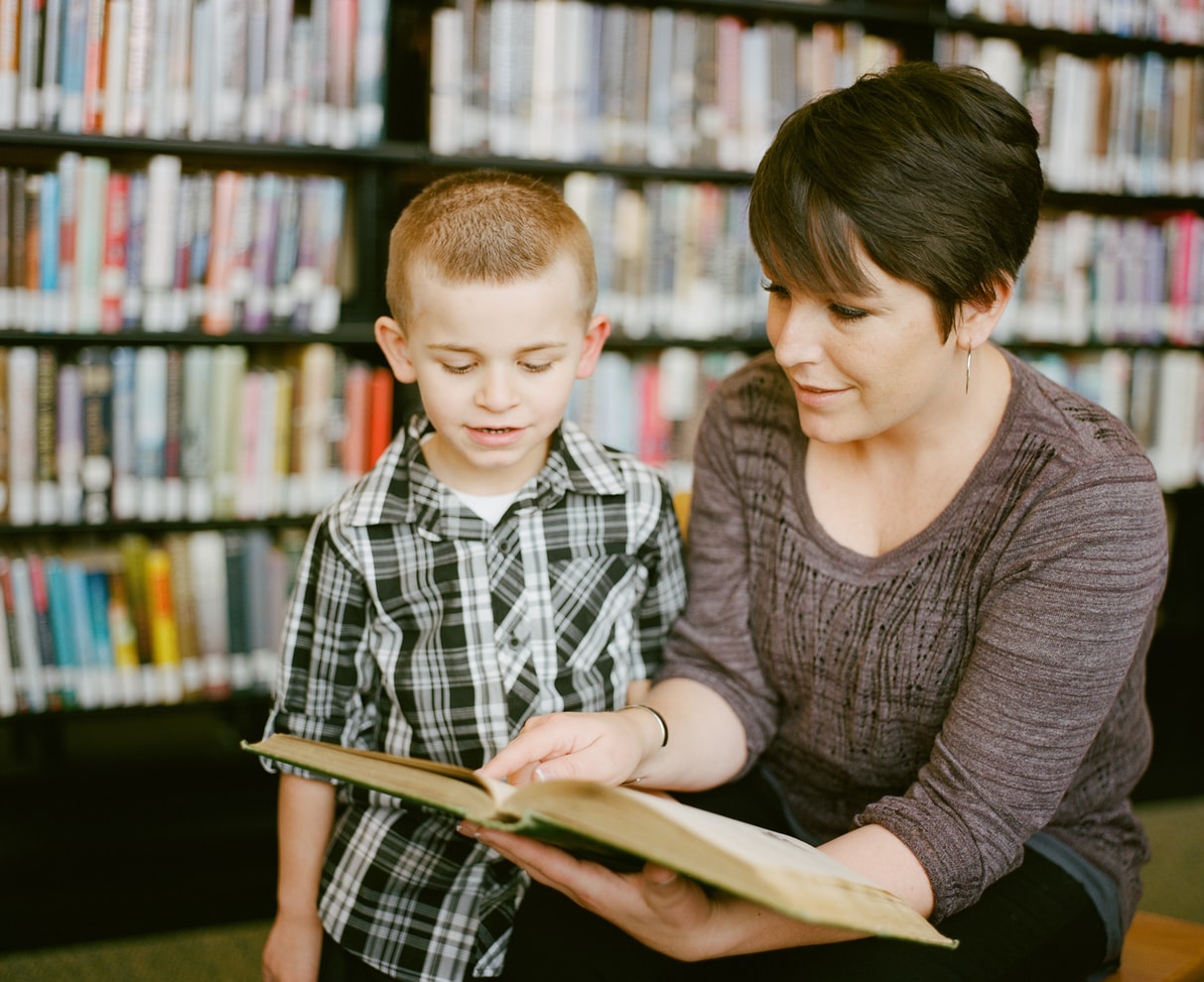 woman helping little boy to read with a backdrop of books in a library